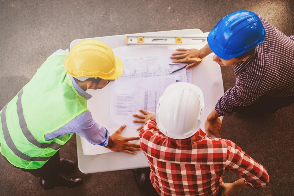 Trois professionnels du bâtiment analysent des plans architecturaux sur chantier