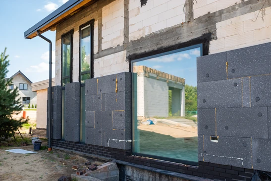 Ouvrier en &eacute;quipement de protection appliquant un isolant thermique sur fa&ccedil;ade ext&eacute;rieure