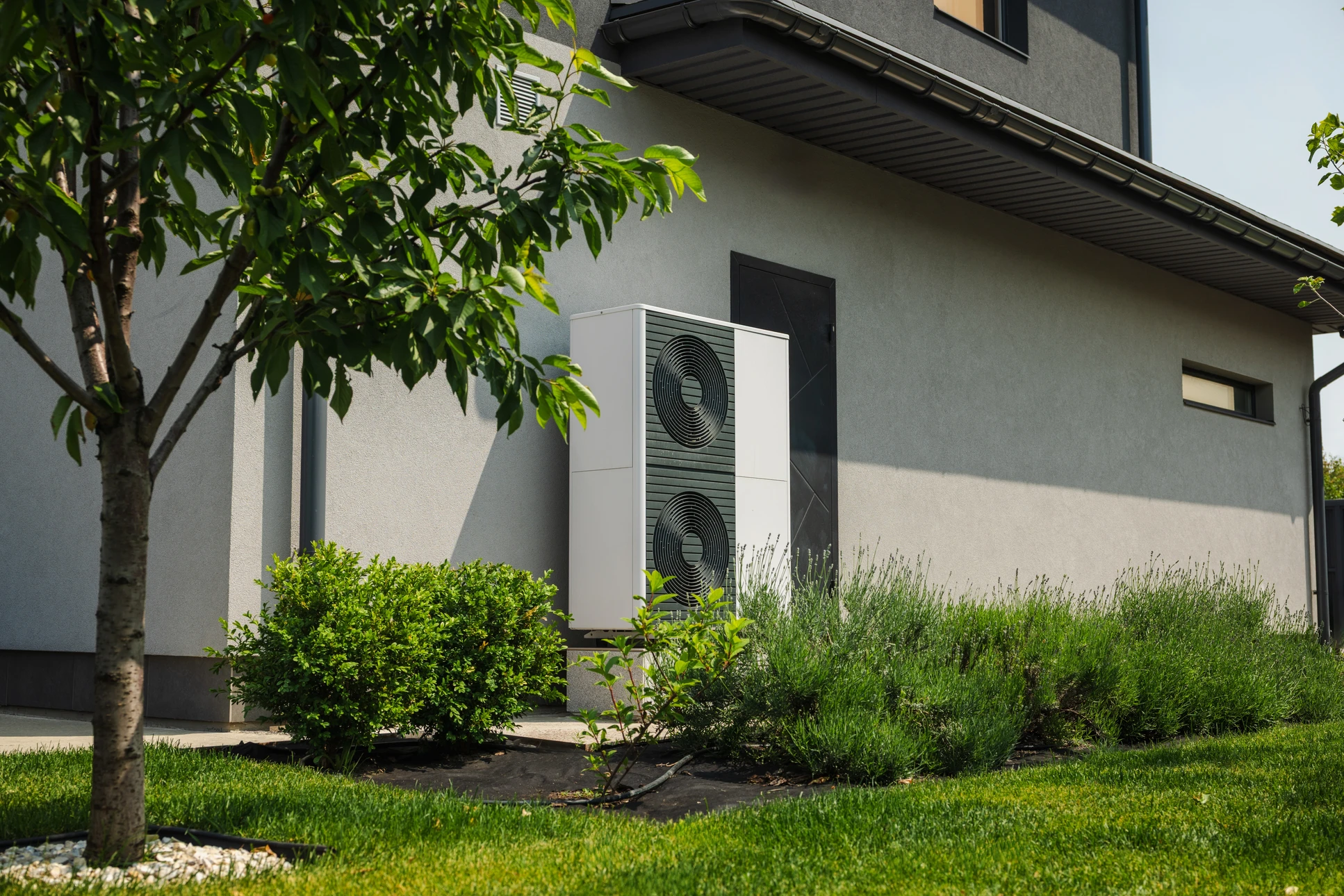 Façade de maison moderne avec unité extérieure de pompe à chaleur air-eau installée sur terrasse carrelée